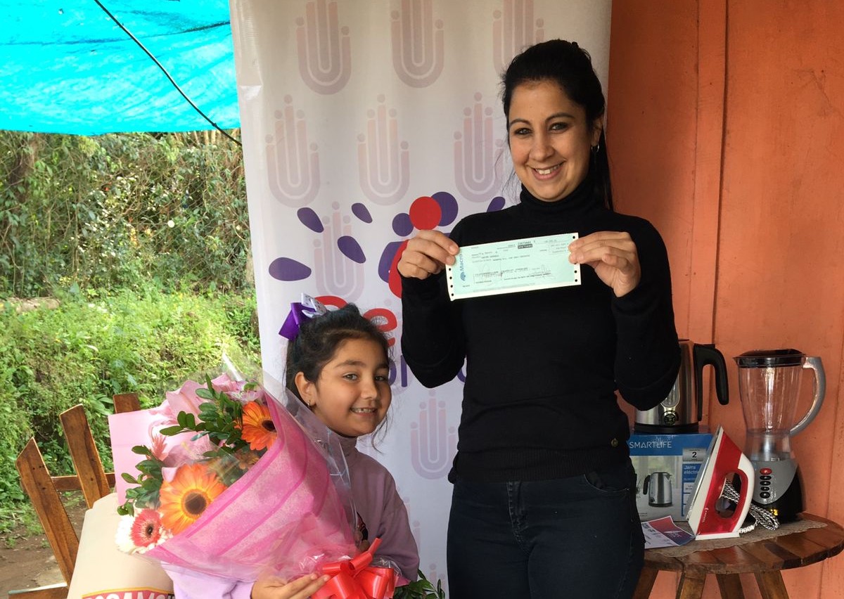 Rafaela Patiño muestra su cheque y premios junto a su hija que sostiene un ramo de flores