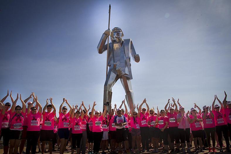 maratonistas aplauden manos arriba, con remeras rosas alusivas a la prevención del cáncer de mamas y la escultura de Andres Guaçurarí de fondo