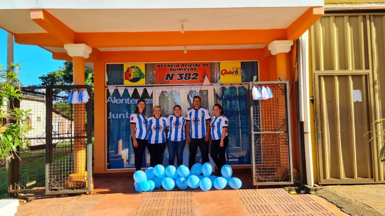 propietarios y empleados de la agencia con sus camisetas de la selección y globos celestes posan frente a la agencia