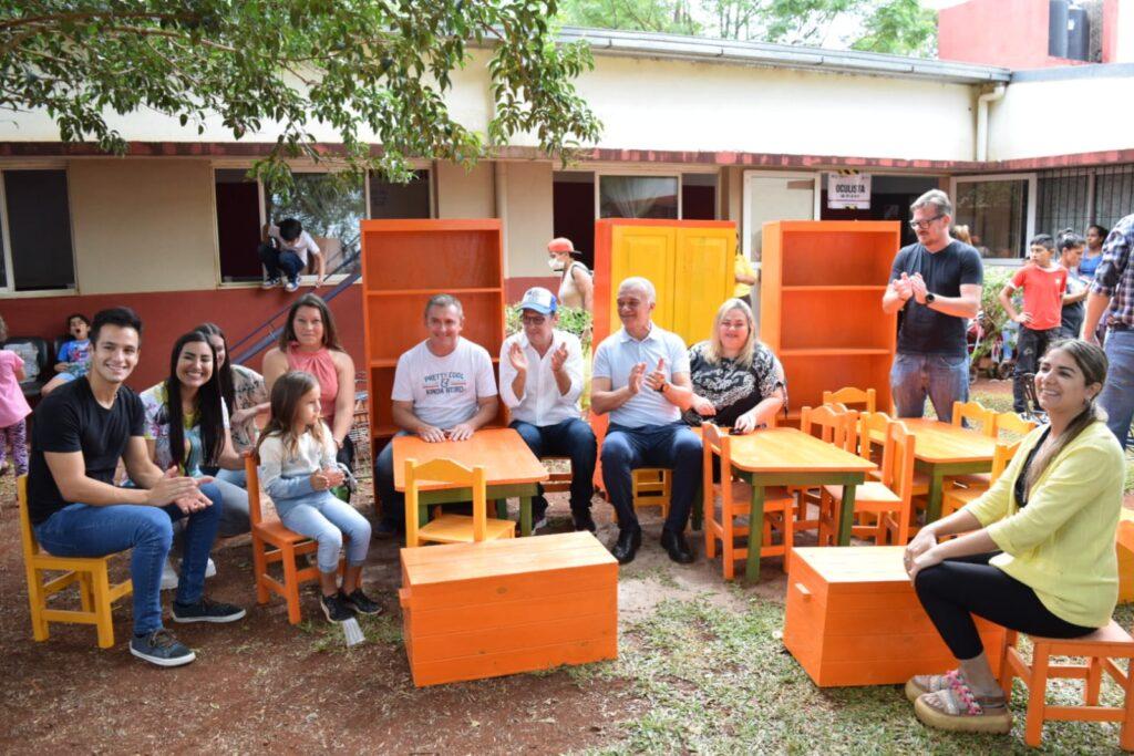 niños, docentes e integrantes de IPLyC Social sonríen y aplauden sentados en el mobiliario escolar