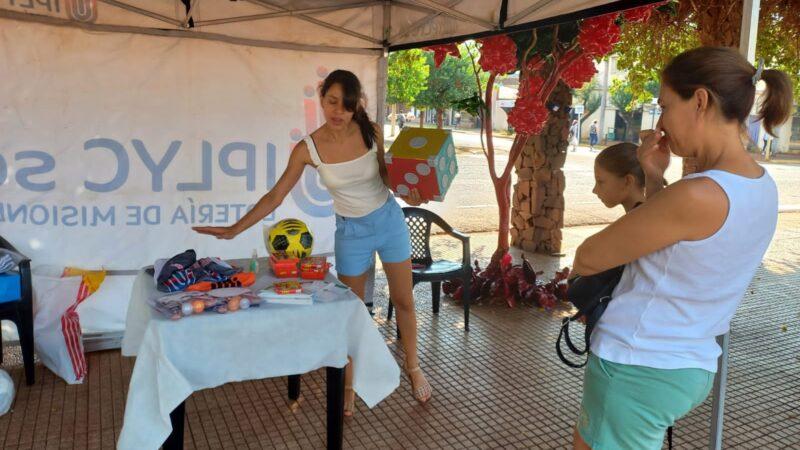 responsable de Juego Responsable, explica un juego de dados a una mamá con su hija que se acercaron al stand