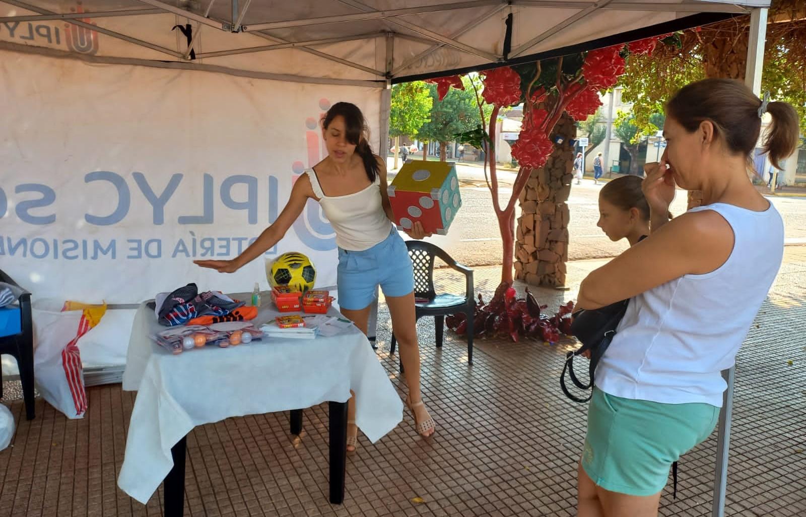 responsable de Juego Responsable, explica un juego de dados a una mamá con su hija que se acercaron al stand