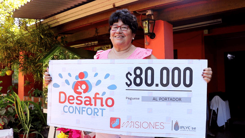 Cristina muestra sonriente su cheque, frente a su casa