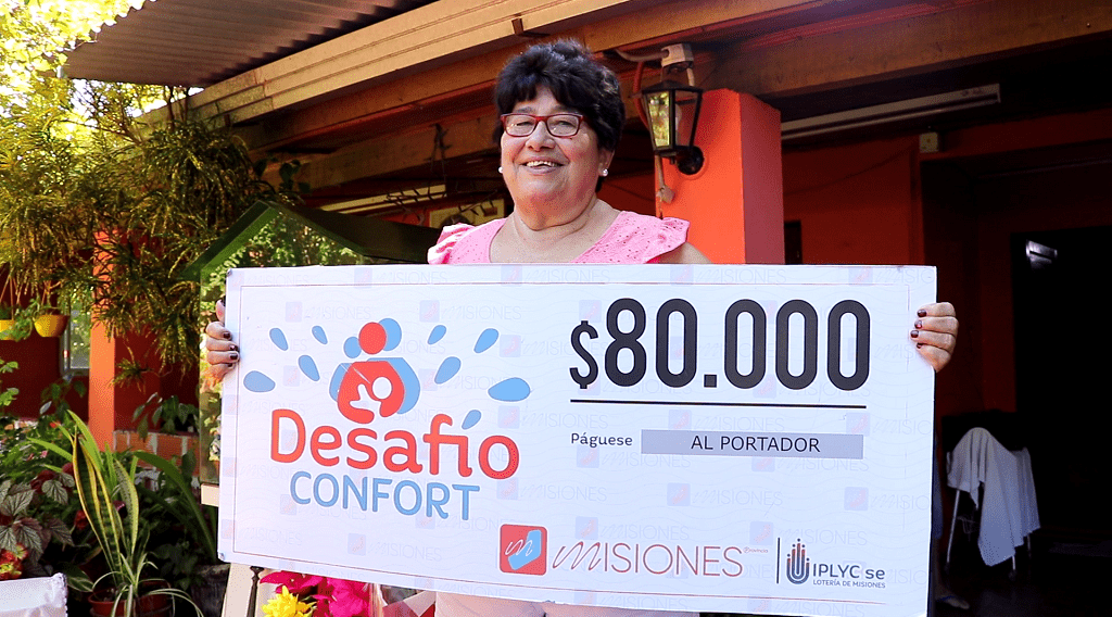 Cristina muestra sonriente su cheque, frente a su casa
