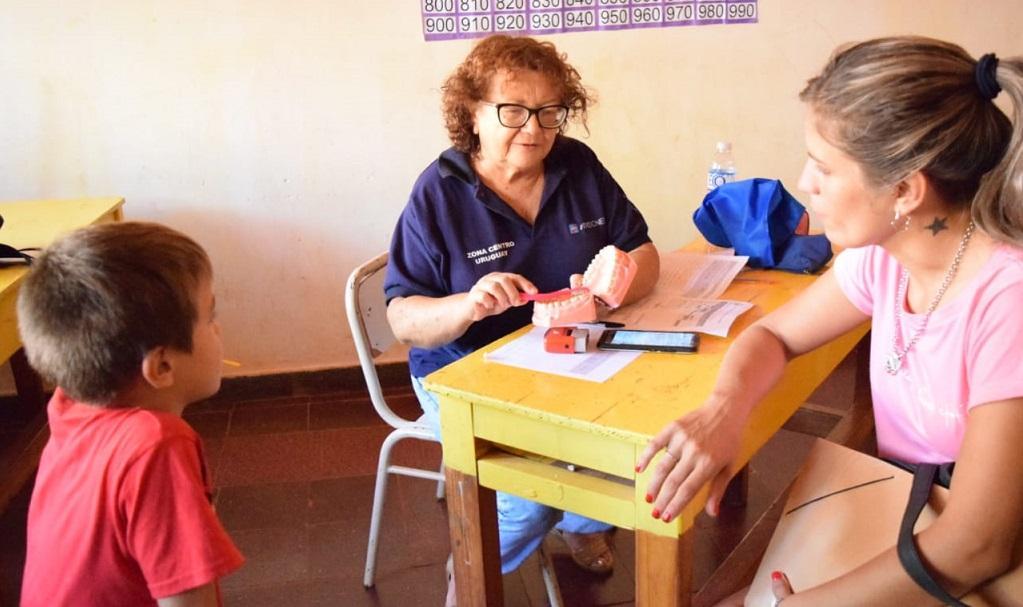 odontóloga enseña a un niño y su mamá cómo cepillarse los dientes con una dentadura didáctica