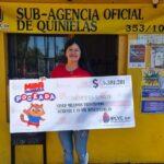 vendedora de la Mini Poceada millonaria frente a la sub agencia muestra sonriente el cheque
