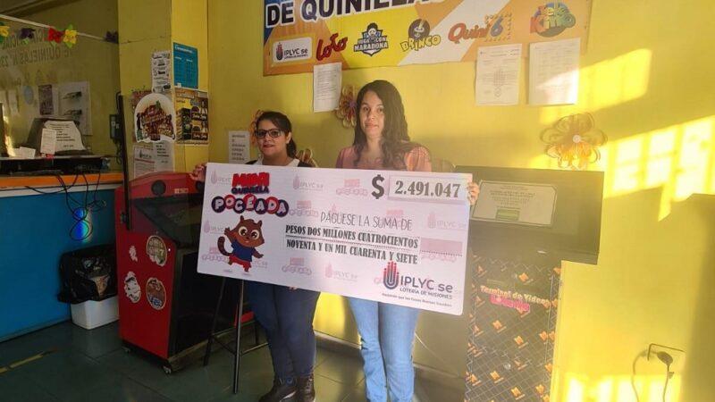 Raquel Moreira y Natalia Munaretto muestran cheque gigante del primer premio de la Mini Poceada, en el local de la Agencia.