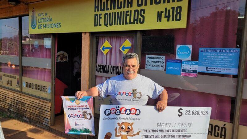 Elvio Maggiolo frente a su agencia muestra sonriente el cheque ganador de la Poceada que ganó su cliente.