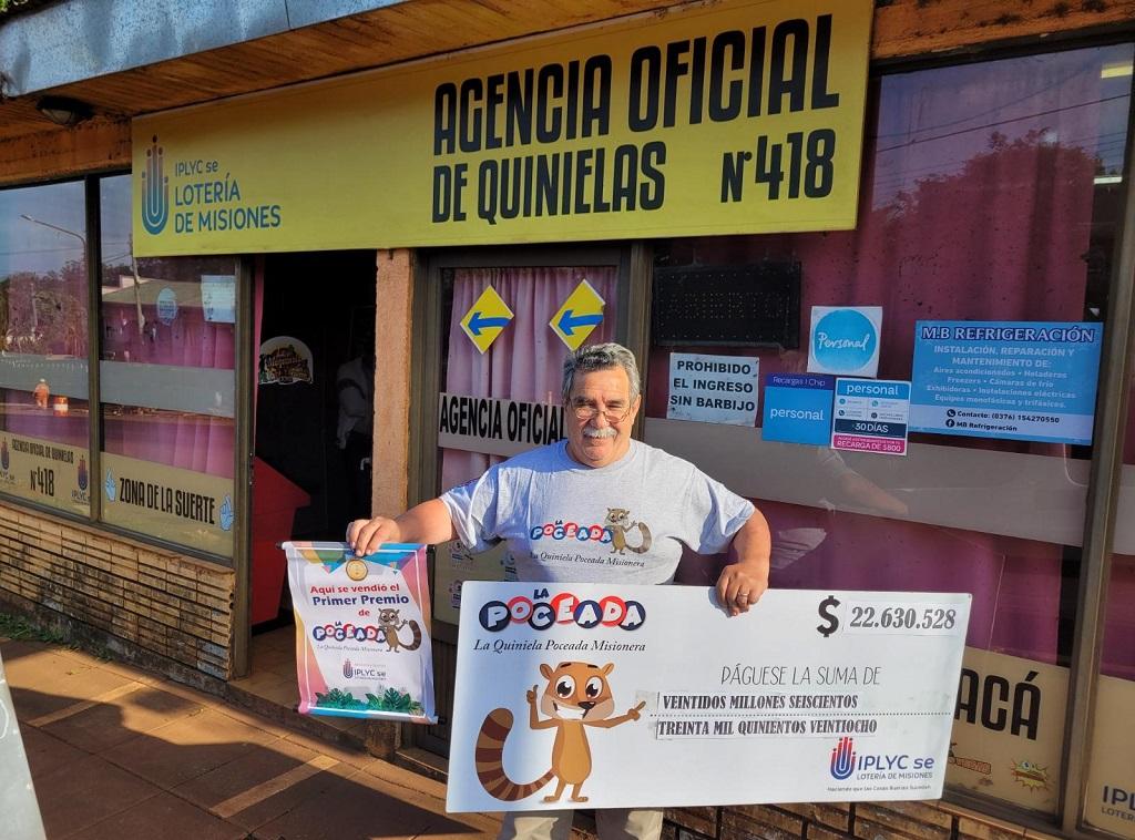 Elvio Maggiolo frente a su agencia muestra sonriente el cheque ganador de la Poceada que ganó su cliente.