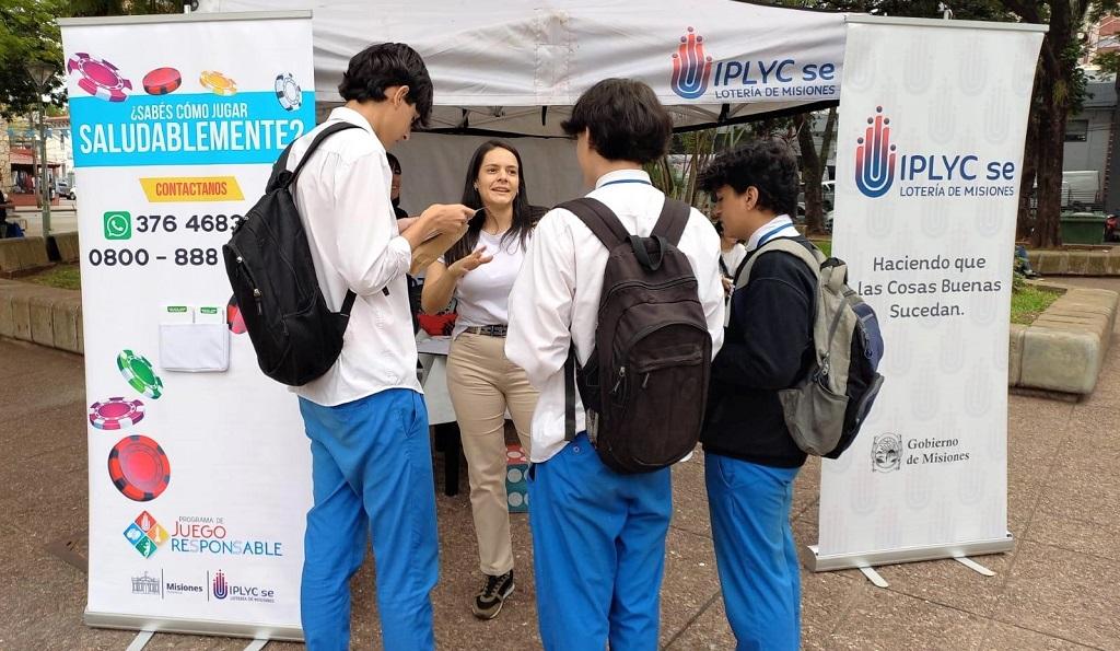 Tres chicos con uniforme escolar escuchan a una de las responsables del Programa de Juego Responsable, en su stand en la Plaza San Martín de Posadas.