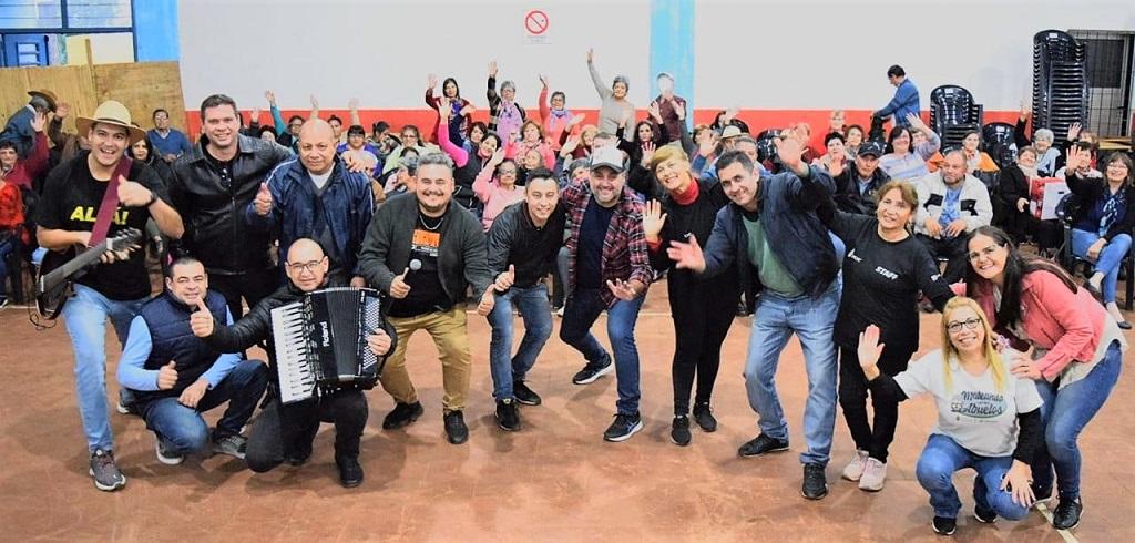 Equipo de IPLyC Social al frente y abuelos detrás saludan a la cámara, en este emotivo encuentro en Salto Encantado.