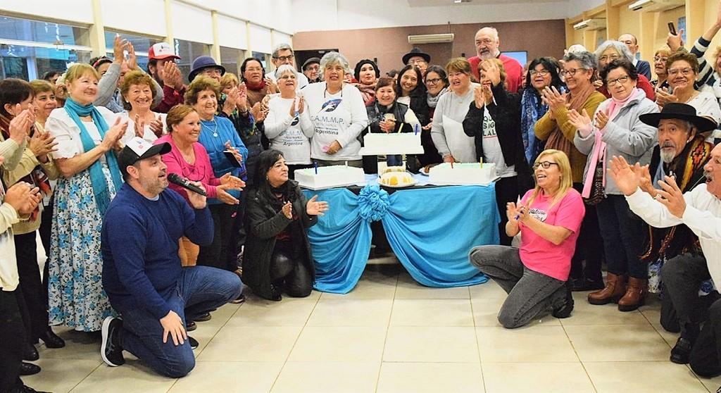 Abuelos que participaron del encuentro festejan y aplauden alrededor de una mesa con tortas y dulces.