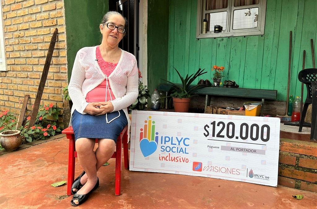 Verónica Gutiérrez muestra su cheque sonriente sentada frente a su casa.