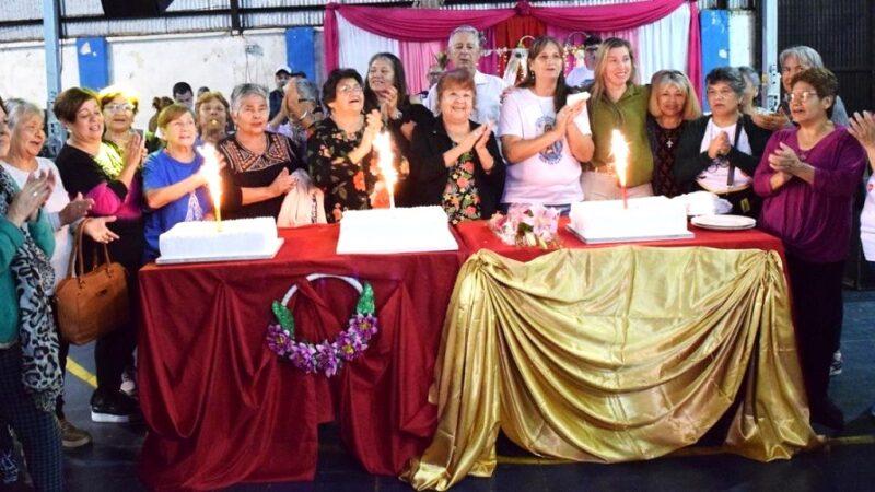 Abuelos cantan feliz cumpleaños alrededor de una mesa con tres tortas con velas encendidas.