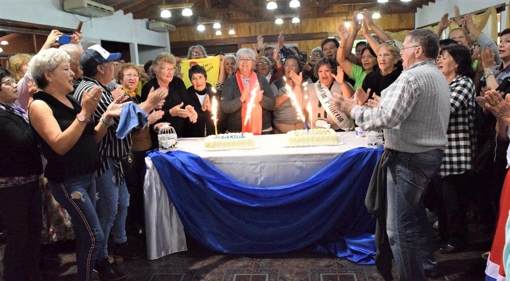 Reunión de abuelos en Eldorado. Abuelos cantan y aplauden alrededor de una mesa con tortas con velas encendidas.