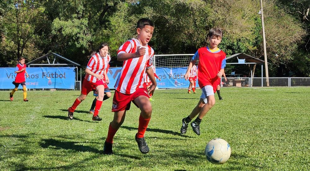 Niño corre tras la pelota secundado por otros de su equipo y el equipo adversario.