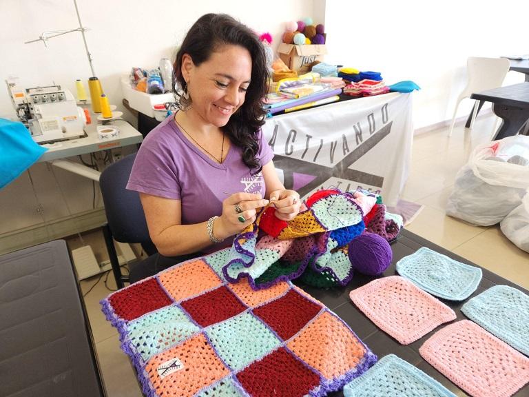 Voluntaria confecciona una manta uniendo cuadros tejidos en crochet.