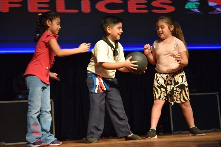 Tres niños realizan juego de pase de pelota sobre el escenario.