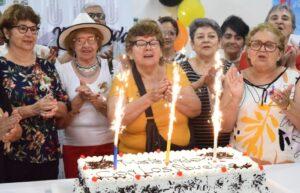 Abuelos cantan felíz cumpleaños alrededor de una torta con velas encendidas, durante una apasionante fiesta.