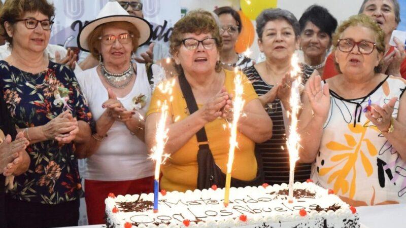 Abuelos cantan felíz cumpleaños alrededor de una torta con velas encendidas, durante una apasionante fiesta.