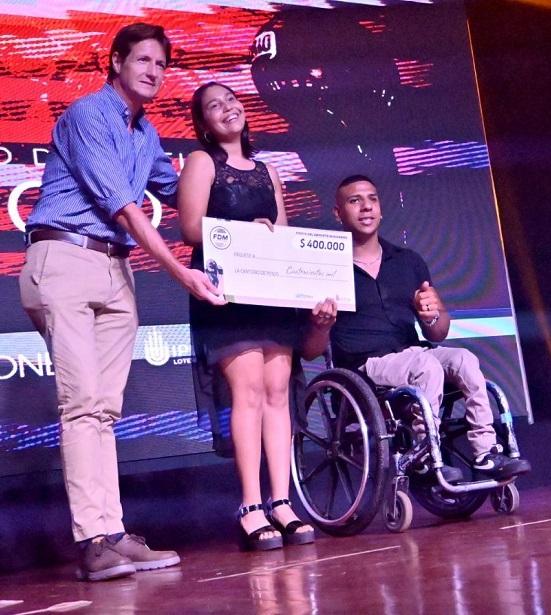 Dos deportistas reciben cheque de becas al deporte adaptado, de manos de Héctor Decut.