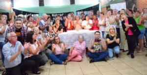 Fiesta de abuelos alrededor de una mesa con tortas cantan y hacen palmas.