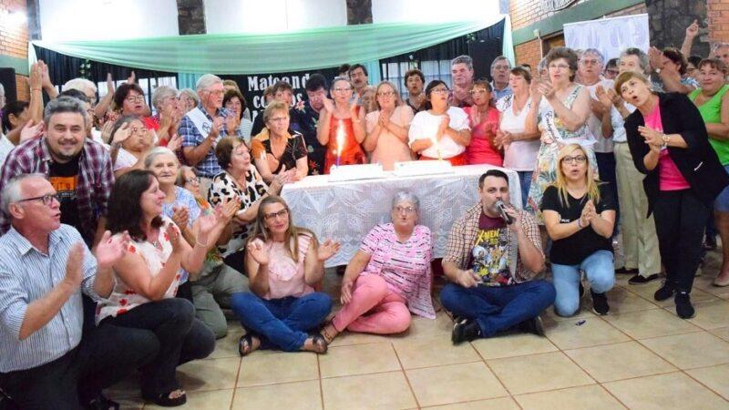 Fiesta de abuelos alrededor de una mesa con tortas cantan y hacen palmas.