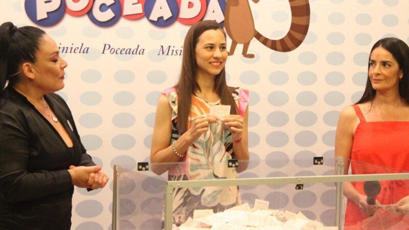 Una joven extrae un cupón durante el sorteo, junto a la conductora y la escribana.
