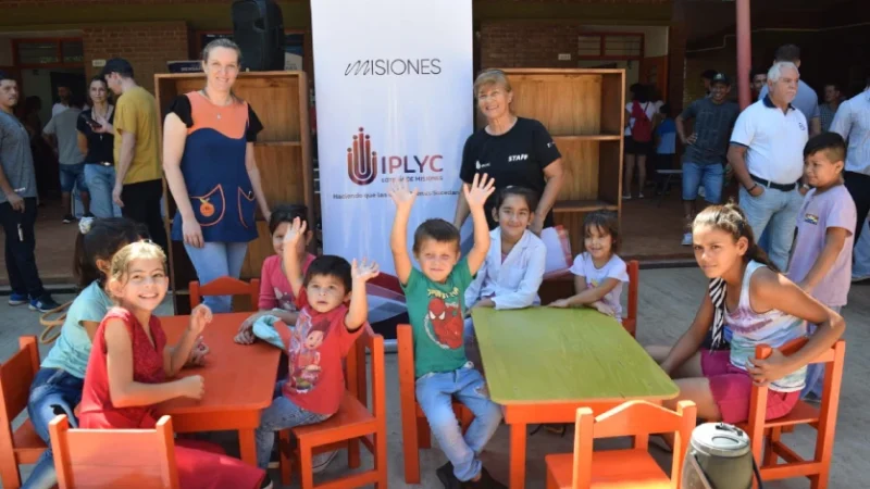 Niños disfrutando el mobiliario escolar junto a su maestra.