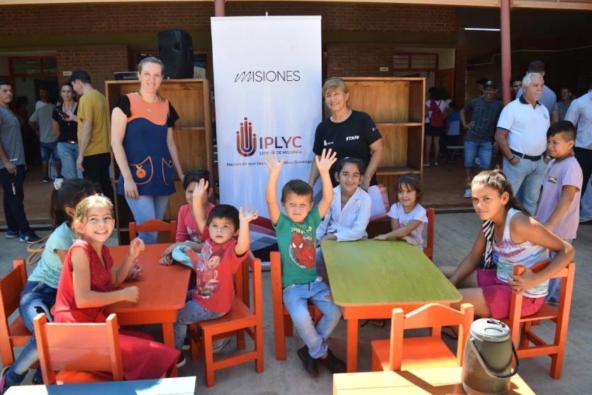 Niños disfrutando el mobiliario escolar junto a su maestra.