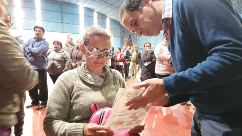 Señora con lentes de prueba óptica lee un texto, asistida por oftalmólogo. Operativo Mirar Mejor en San Javier.