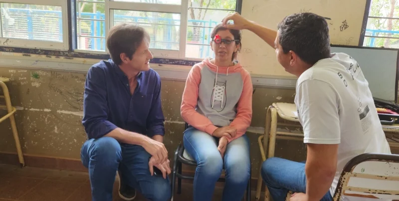 Héctor Decut observa a oftalmólogo probando graduación con lentes de prueba óptica a una joven. Mirar Mejor - San Ignacio.