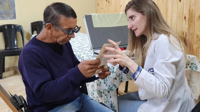 Oftalmóloga ayuda a leer a un vecino con lentes graduados. Mirar Mejor en Colonia Alberdi.
