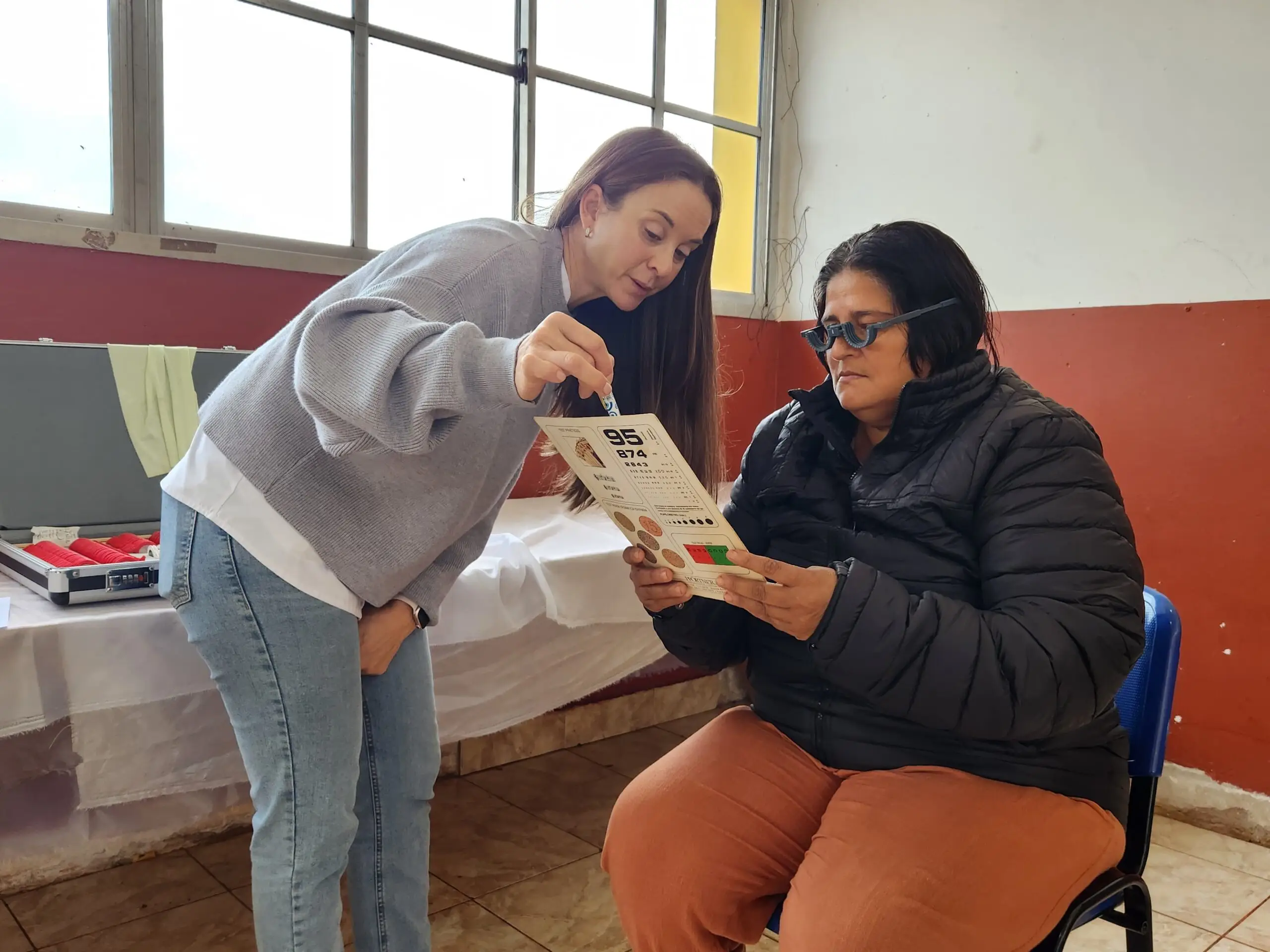 Oftalmologa ayuda a una vecina a leer con lentes de prueba. Mirar Mejor en Guaraní.
