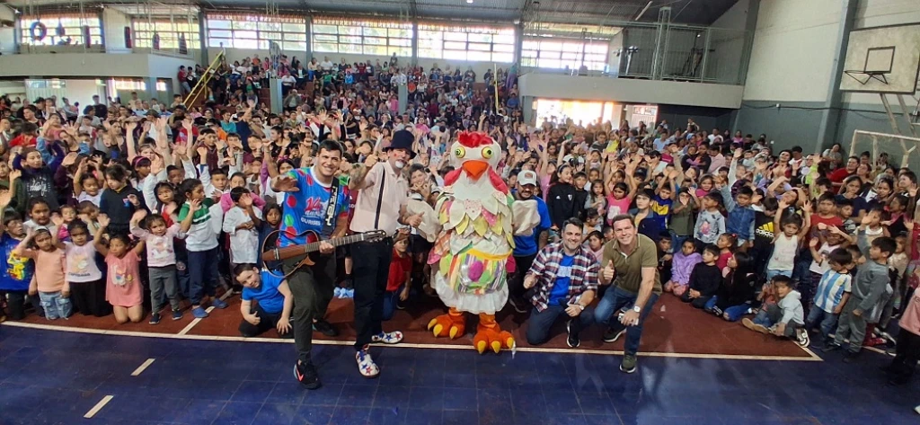 Equipo de Gurises Felices y una multitud de niños saludan felices a la cámara.