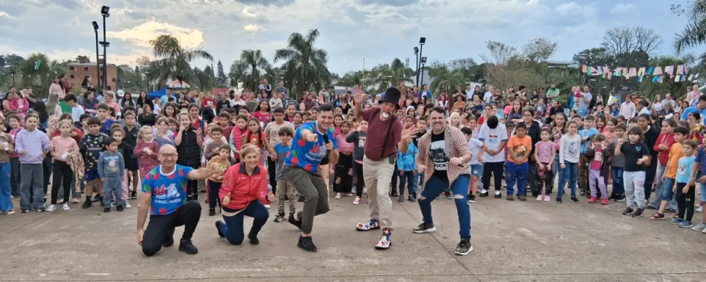 Equipo de Gurises Felices y una multitud de público infantil saludan a cámara en Alem.