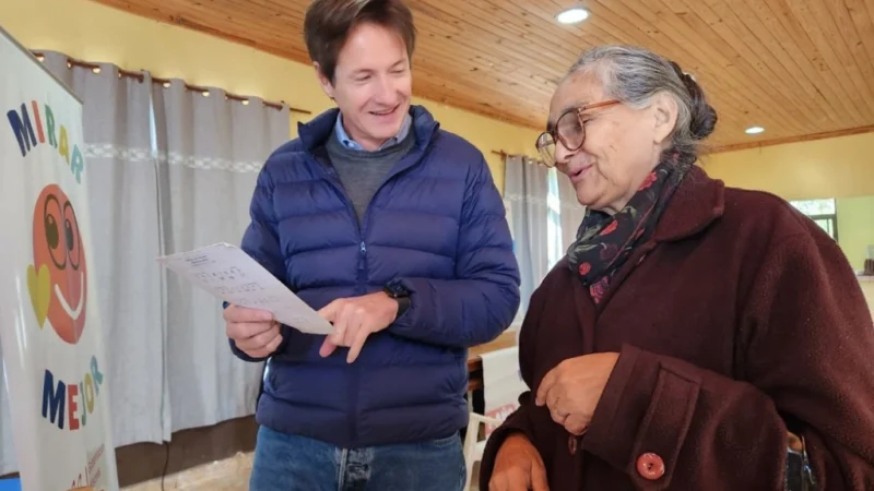 Héctor Decut le toma lectura a una señora mayor muy sonriente con sus nuevos lentes. Mirar Mejor - San Martín.