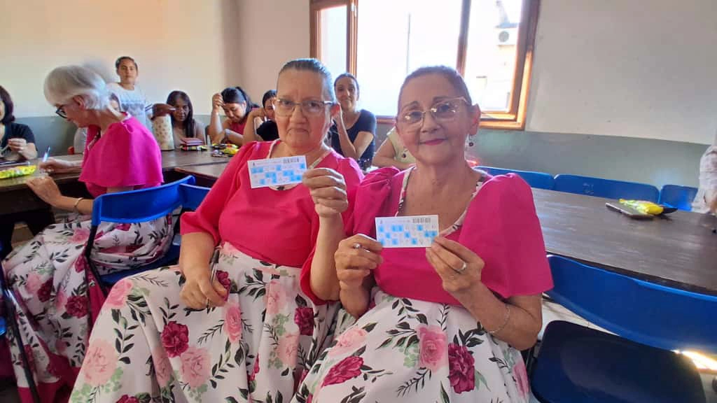 2 abuelas vestidas con sus trajes folclóricos con sus cartones de bingo.