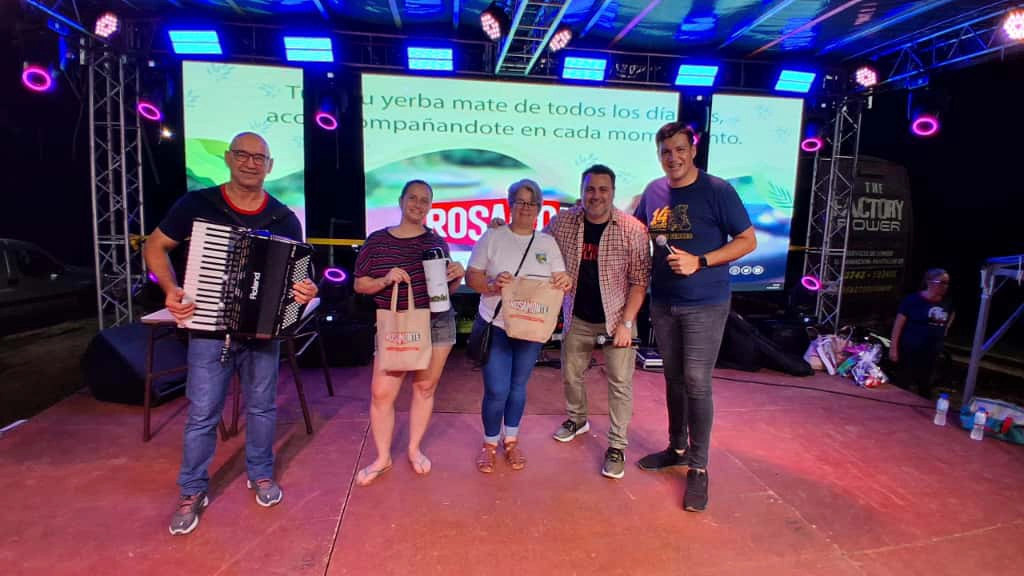 Equipo de Gurises junto a dos señoras que reciben un obsequio, sobre el escenario.