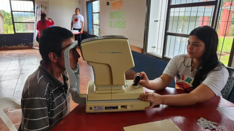 Vecino recibe atención oftalmológica por parte de una profesional del programa mediante un autorefractómetro.