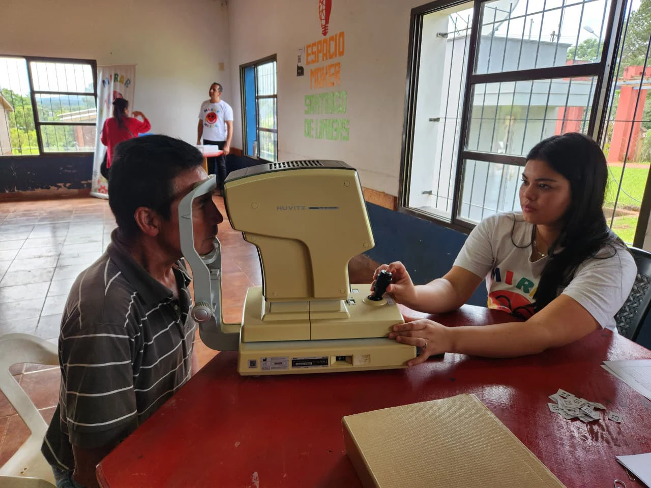 Vecino recibe atención oftalmológica por parte de una profesional del programa mediante un autorefractómetro.
