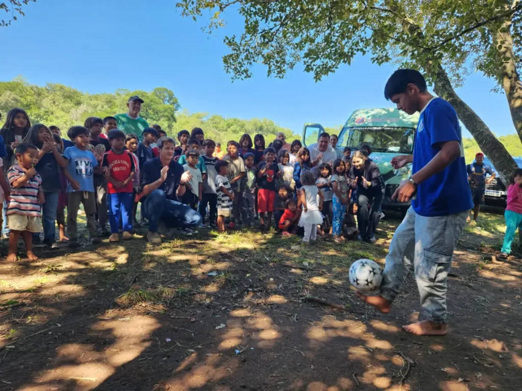 Un niño de la aldea participa haciendo jueguitos con la pelota aplaudido por los demás niños.
