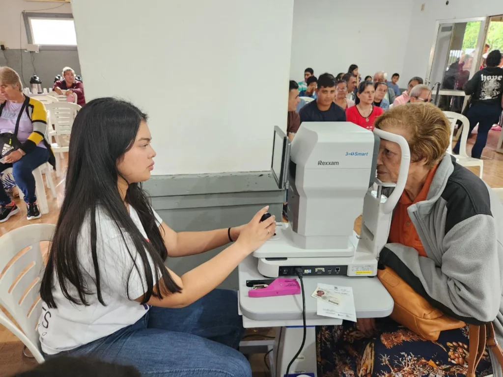 Oftalmóloga revisa los ojos de una vecina mediante un autorefractómetro.