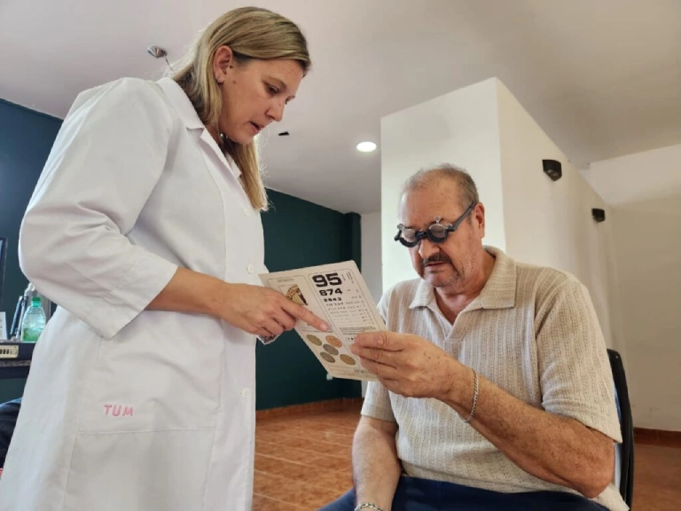 Vecino mayor lee un texto con lentes de prueba con ayuda de oftalmóloga. Mirar Mejor - Apóstoles.