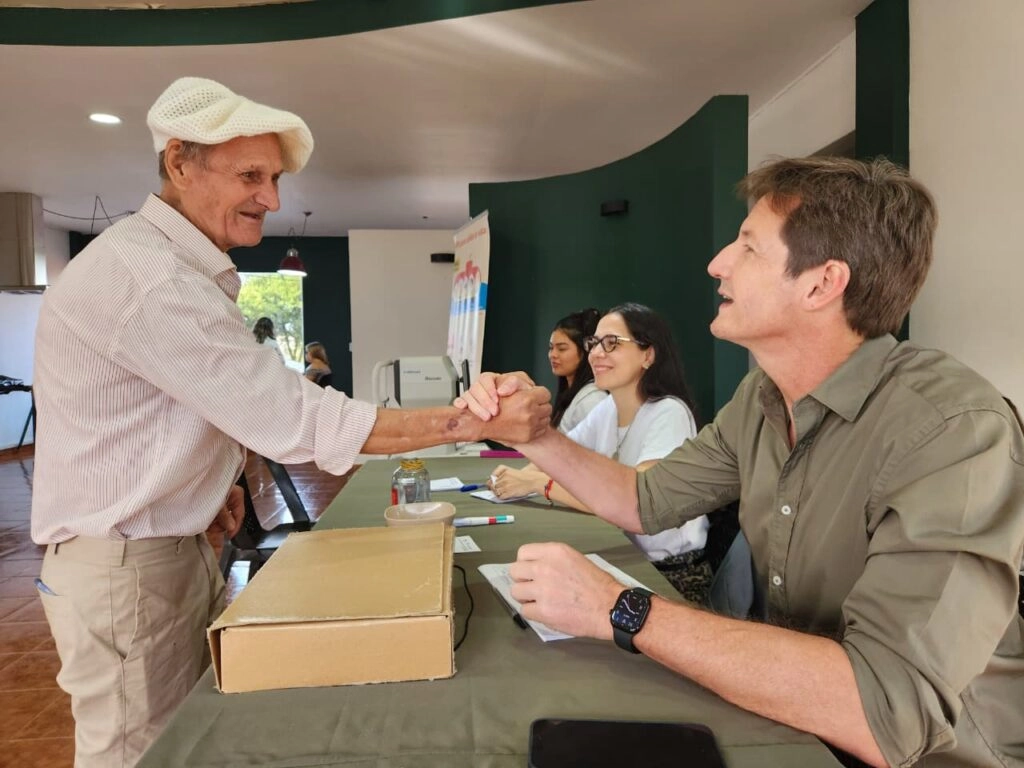 Héctor Decut y un vecino mayor se saludan con un un apretón de manos. Mirar Mejor - Apóstoles.