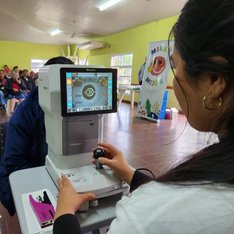 Oftalmóloga revisa los ojos de una joven vecina mediante un autorefractómetro.