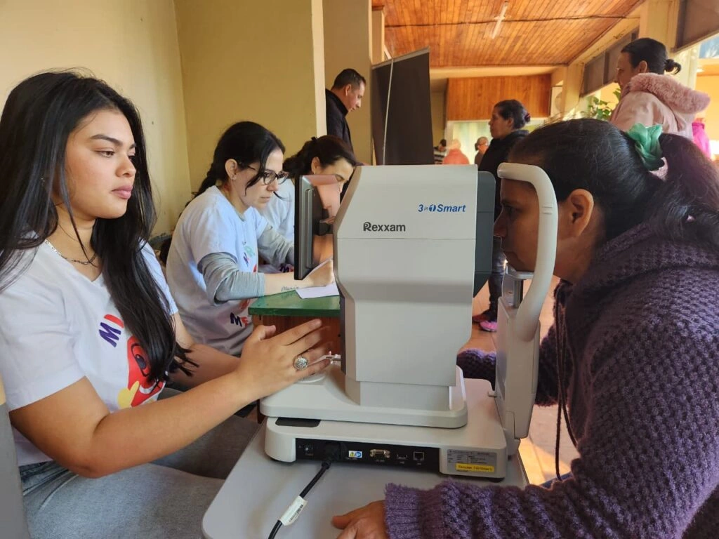 Oftalmóloga revisa los ojos de una joven vecina mediante un autorefractómetro.