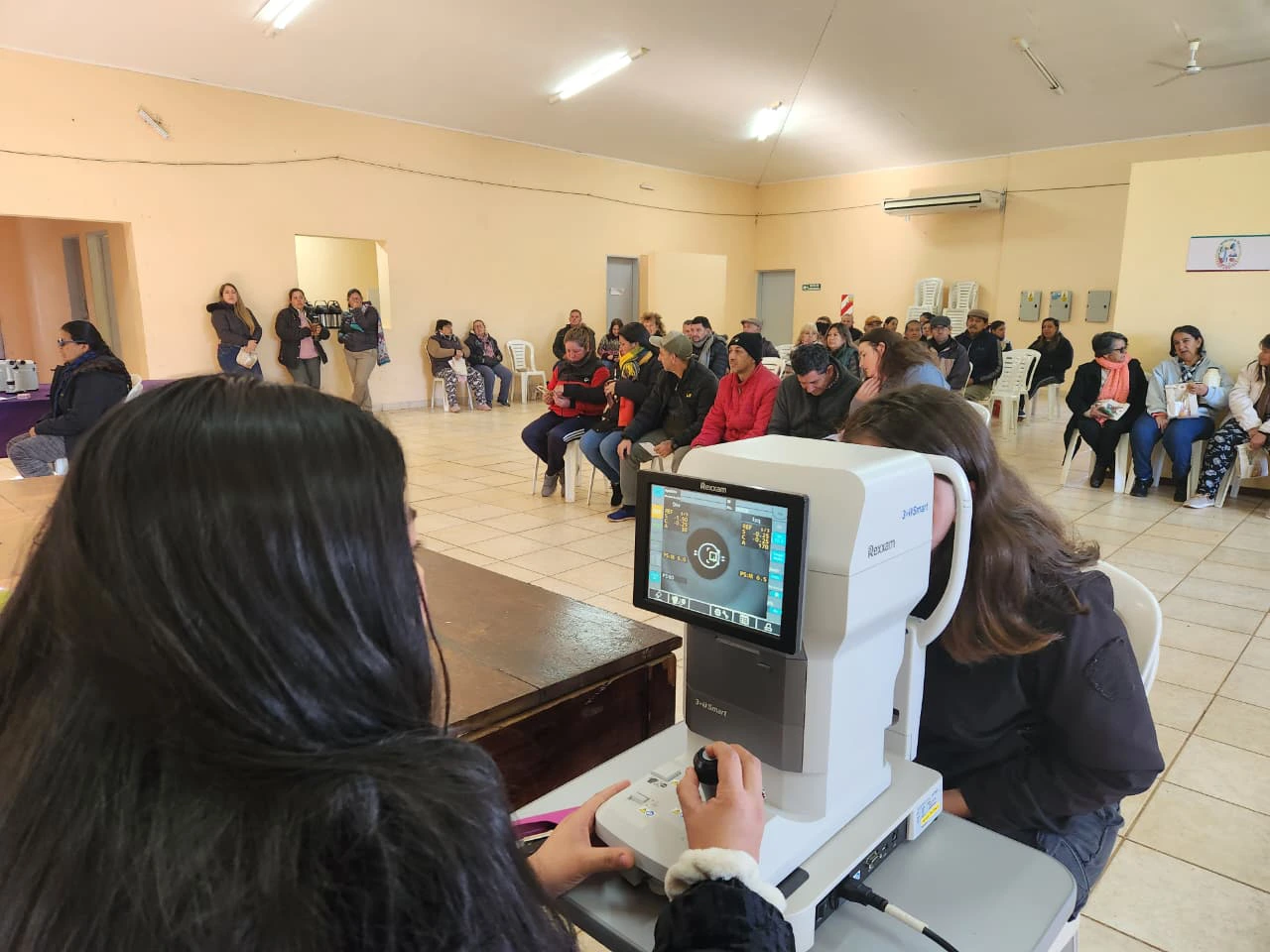 Oftalmóloga revisa los ojos de una vecina mediante un autorefractómetro. Mirar Mejor en Profundidad.