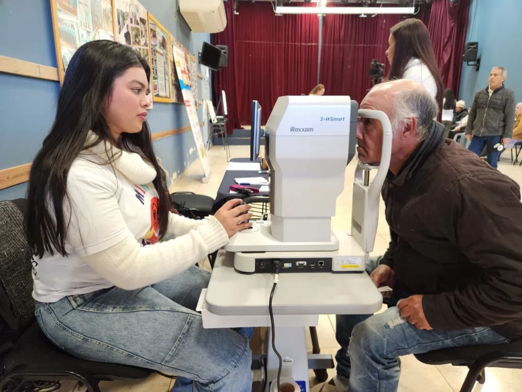 Oftalmóloga revisa los ojos de un vecino mayor mediante un autorefractómetro. Mirar Mejor en Santo Pipó.
