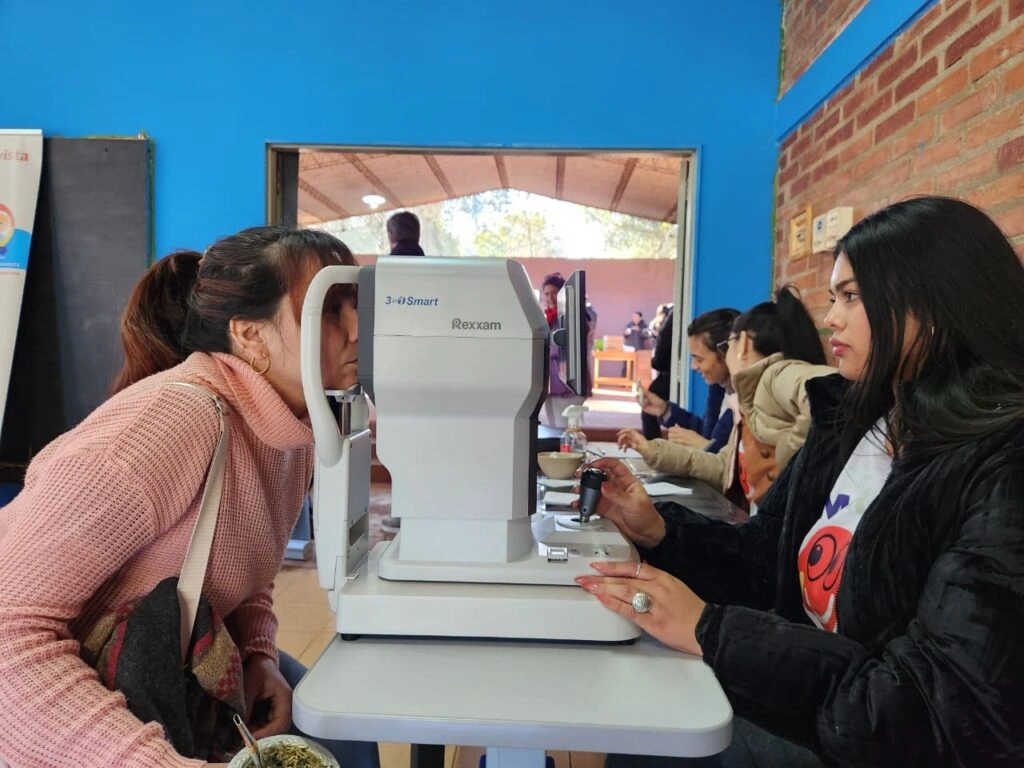 Oftalmóloga revisa los ojos de una vecina mediante un autorefractómetro.